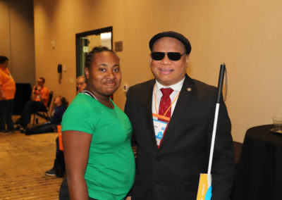 Ollie cantos and conference participant pose and smile together for a picture. He is dressed in a suit and she is dressed in a green shirt.