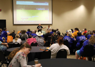 A crowd of listeners is pictured sitting around tables and listening to featured presenter Garrett Holeve.