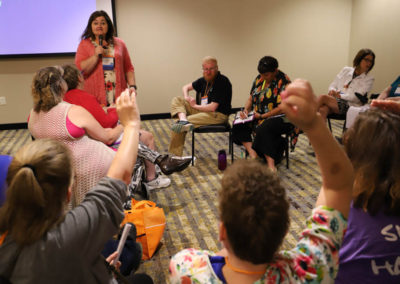 Breakout presenter holds microphone and answers listeners' questions while others raise hands.