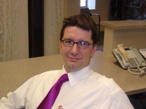 Photo of Brad Muerrens. He is sitting in frnt of a desk and smiling.