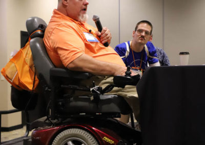 Brad Linnenkamp, Kansas self-advocate leader, speaks into microphone as he speaks to a crowd of conference attendees