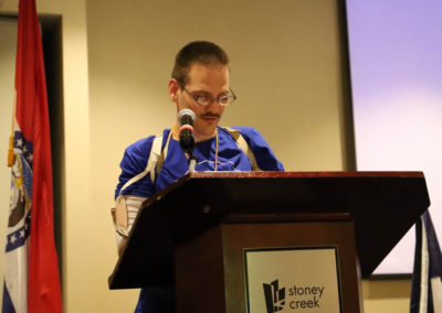 Travis Schaffer, self-advocate from Nebraska, is pictured standing at a podium as he speaks to the SOAR conference Crowd