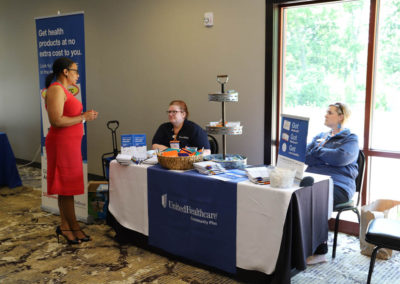 A conference participant stands and talks to the two women seated at the United Healthcare information table.