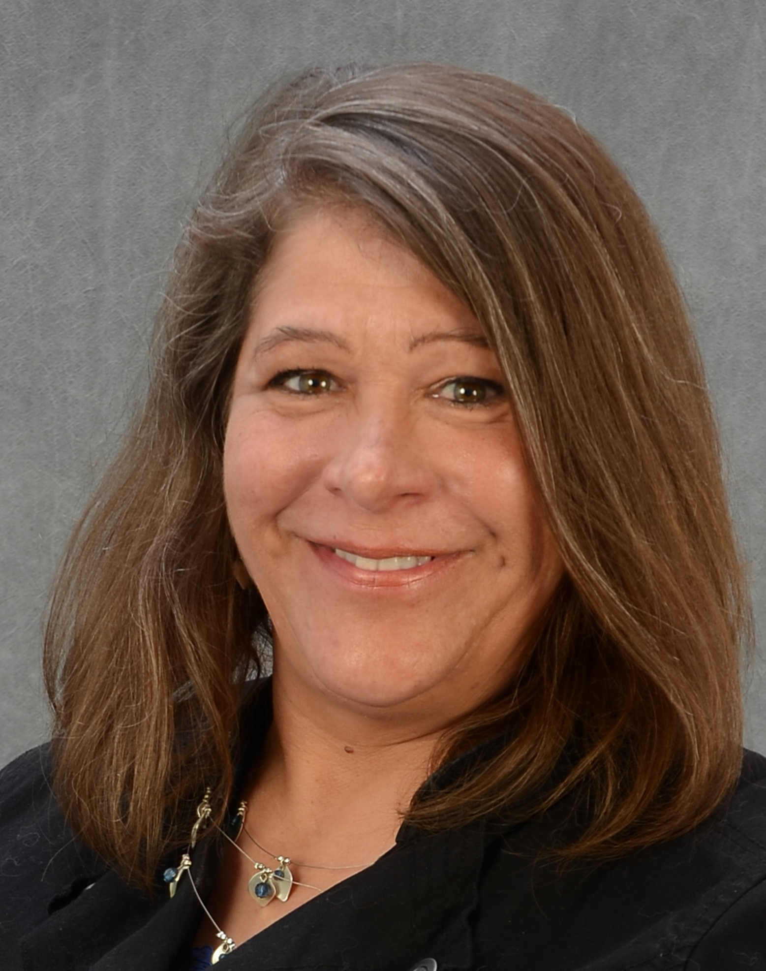 Photo of Chris Stewart. She is standing in front of a grey background and smiling.