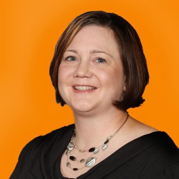 Photo of Jenn Wolff. She is sitting in front of an orange background and smiling.