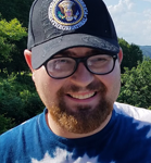 Photo of Brady Werger in front of trees. He is wearing a baseball cap and smiling.