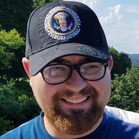 Photo of Brady Werger in front of trees. He is wearing a baseball cap and smiling.