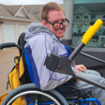 Photo of Michael Martin sitting in a wheelchair. He is looking over his right shoulder and smiling.