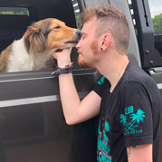 Photo of Michael Gillette next to a pickup truck. He is petting a dog through an open window.